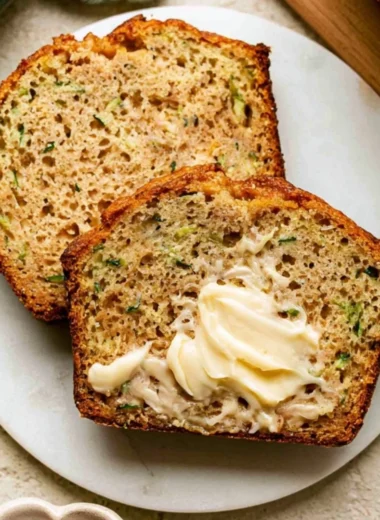 A slice of Greek Yogurt Zucchini Bread on a wooden table, showcasing its moist texture.