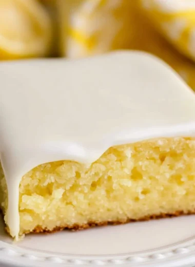A slice of lemonade cake garnished with lemon slices and frosting.