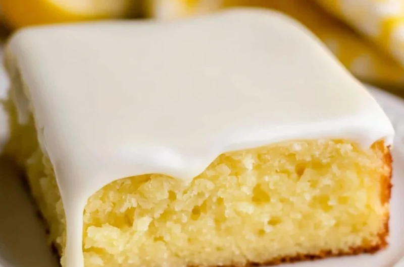 A slice of lemonade cake garnished with lemon slices and frosting.