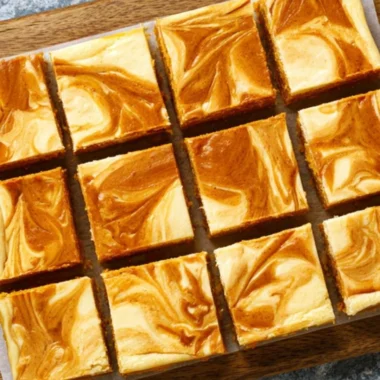 Swirled pumpkin cheesecake bars topped with whipped cream and cinnamon
