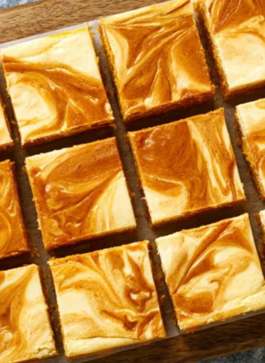 Swirled pumpkin cheesecake bars topped with whipped cream and cinnamon